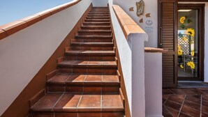 A staircase with a white handrail and brown steps leading to a door with a glass panel and sunflowers. - GuestHost - Cozy detached house of about 60 sqm, perfect for 4 people, located on the ground floor.The property is located in Torre dei Corsari, a charming village overlooking the splendid Costa Verde of Sardinia. In a few minutes by car you can reach so (Torre dei Corsari)