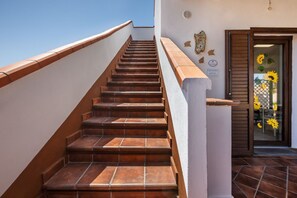 Eine Treppe mit weißer Handlauf und braunen Stufen führt zu einer Tür mit Glasfenster und Sonnenblumen.