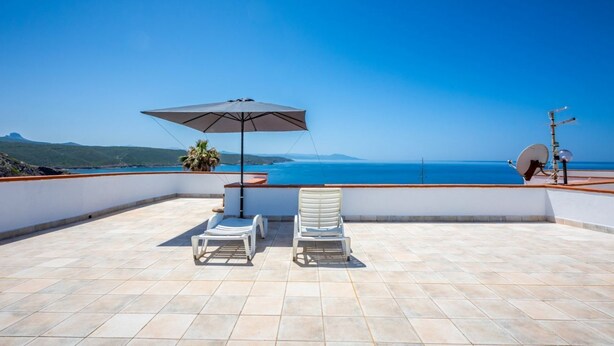 A terrace with two white lounge chairs, a large umbrella, and a satellite dish. - GuestHost - Cozy detached house of about 60 sqm, perfect for 4 people, located on the ground floor.The property is located in Torre dei Corsari, a charming village overlooking the splendid Costa Verde of Sardinia. In a few minutes by car you can reach so (Torre dei Corsari)