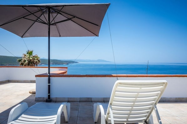 Una terraza con dos sillones blancos, una sombrilla grande y vista al mar.