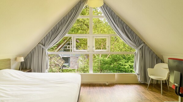 A bedroom with a large window, a bed, a chair, and a desk.