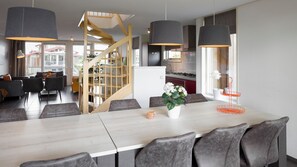 A modern dining area with a long table, grey upholstered chairs, and pendant lighting.
