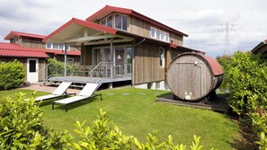 A modern building with a wooden exterior, a covered outdoor area with chairs, and a large barrel in the foreground.