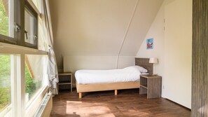 A bedroom with a sloped ceiling, a bed with white bedding, a bedside table with a lamp, and a view through a window.
