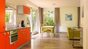A modern kitchen with orange cabinets, a dining area with a table and chairs, and a view of greenery outside.
