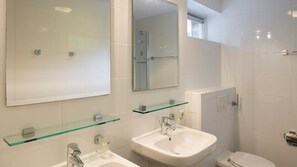 A modern bathroom with two sinks, a glass shelf, a mirror, and a toilet.