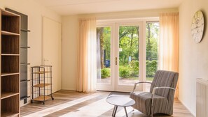 A room with a sliding glass door leading to a garden, a chair, a small table, and a bookshelf.