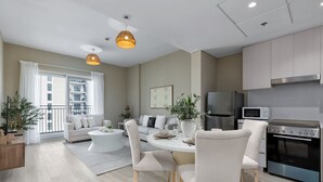 Una sala moderna con sofá, mesa de comedor y sillas, una cocina con electrodomésticos, y un balcón con plantas.