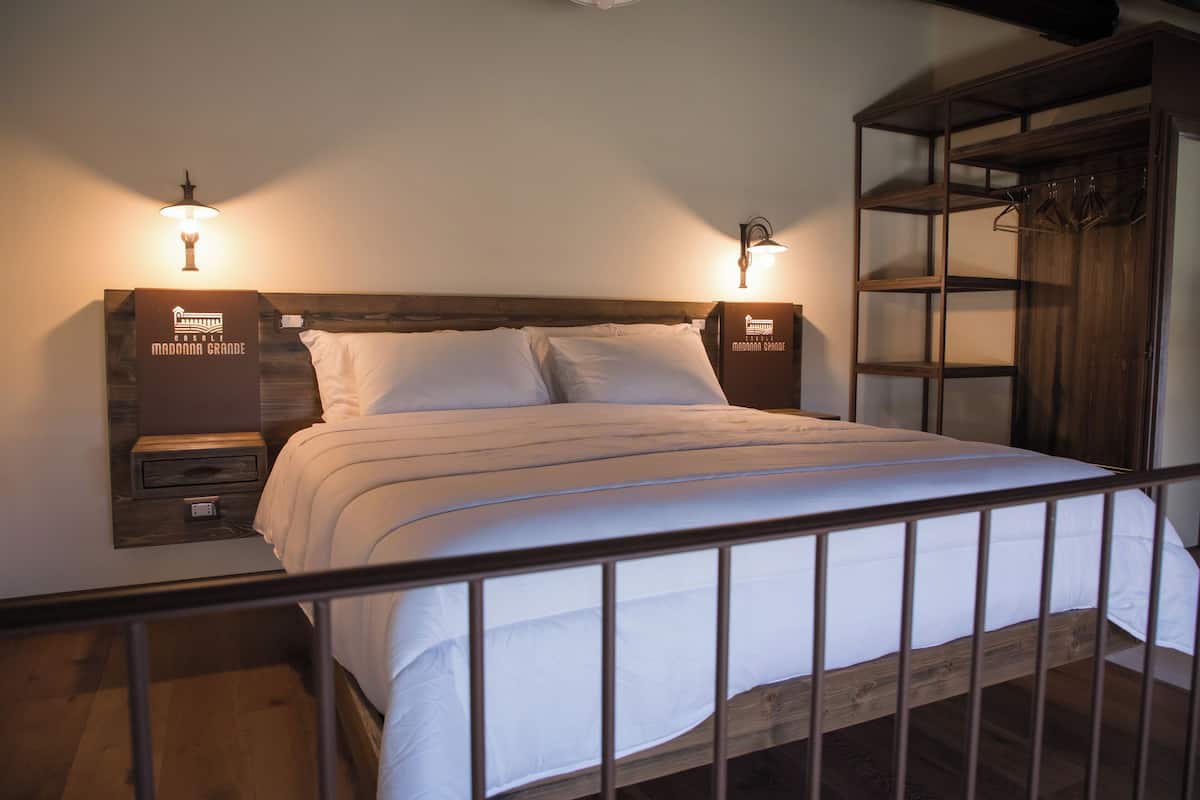 A neatly made bed with a wooden headboard, two bedside tables with lamps, and a wooden wardrobe with a hanging rack.