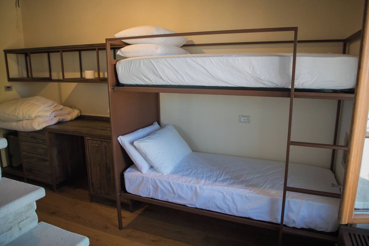 A bunk bed with a wooden frame, white bedding, and a desk with a chair.