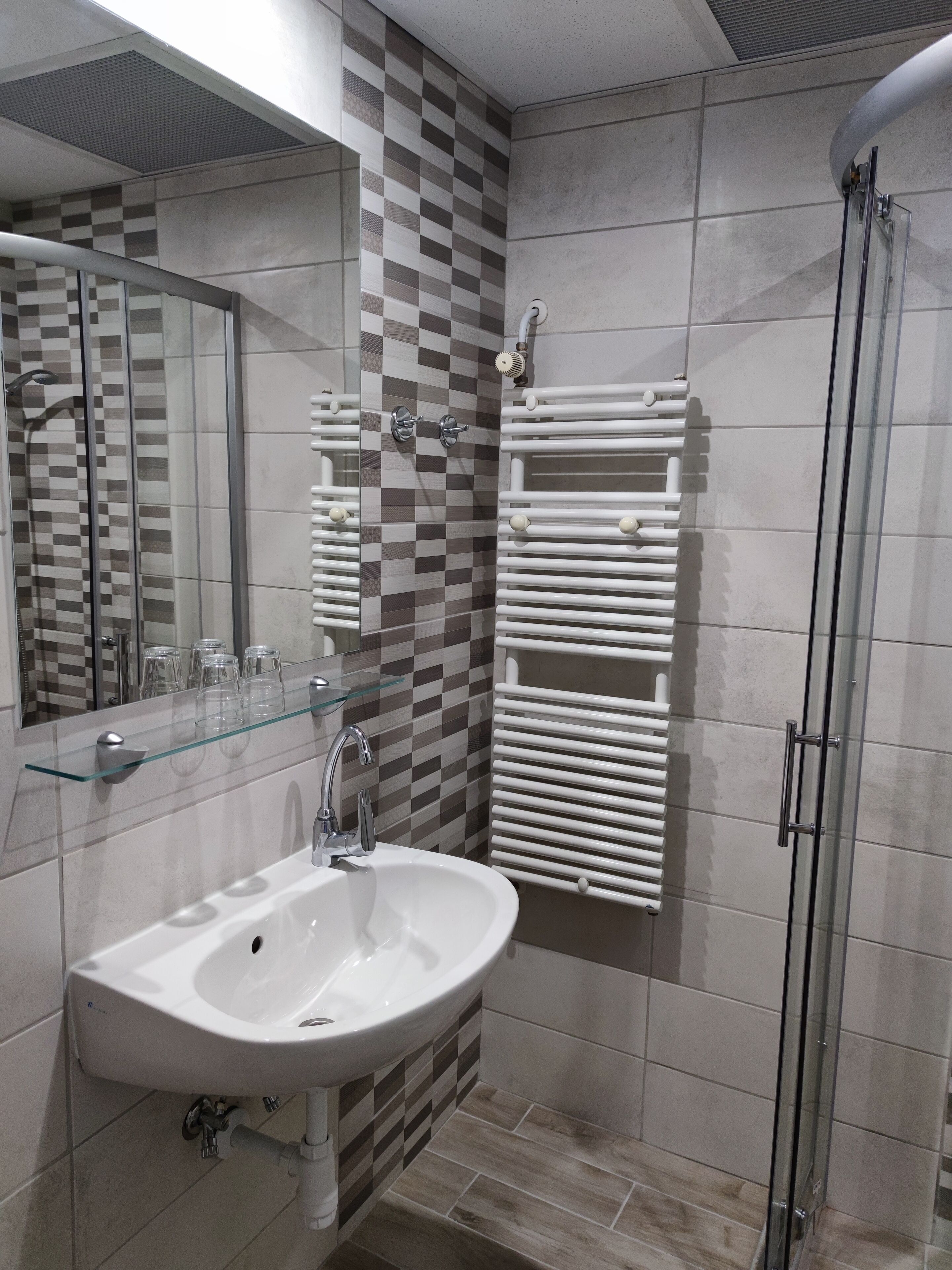 Une salle de bain avec un lavabo blanc, une étagère en verre, un miroir, une douche avec une porte en verre et un porte-serviettes.