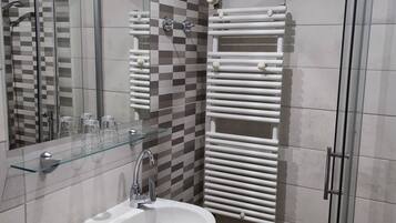A bathroom with a white sink, a glass shelf, a mirror, a shower with a glass door, and a towel rack.