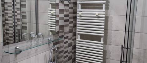 Une salle de bain avec un lavabo blanc, une étagère en verre, un miroir, une douche avec une porte en verre et un porte-serviettes.