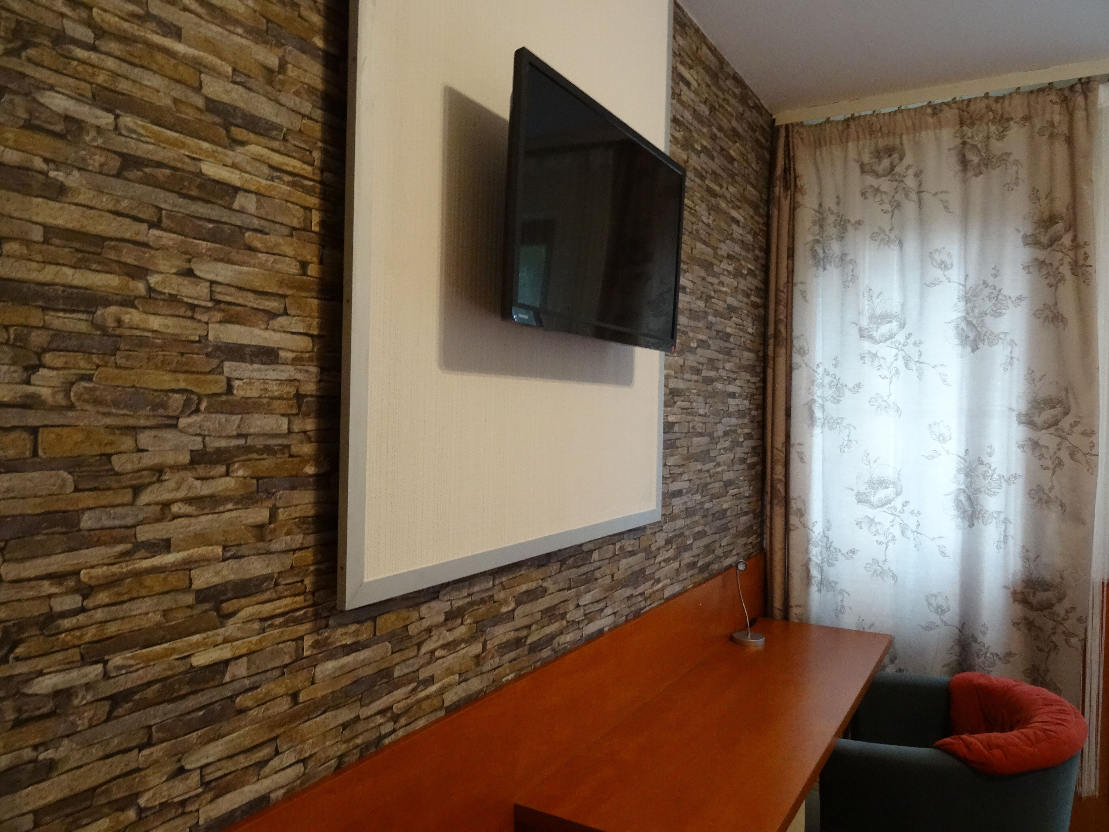 A room with a stone wall, a mounted flat-screen TV, a wooden table, and a chair with a red cushion.