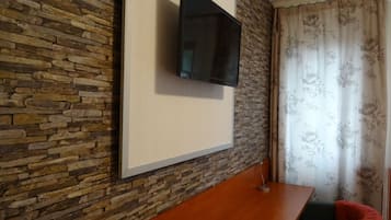 A room with a stone wall, a mounted flat-screen TV, a wooden table, and a chair with a red cushion.