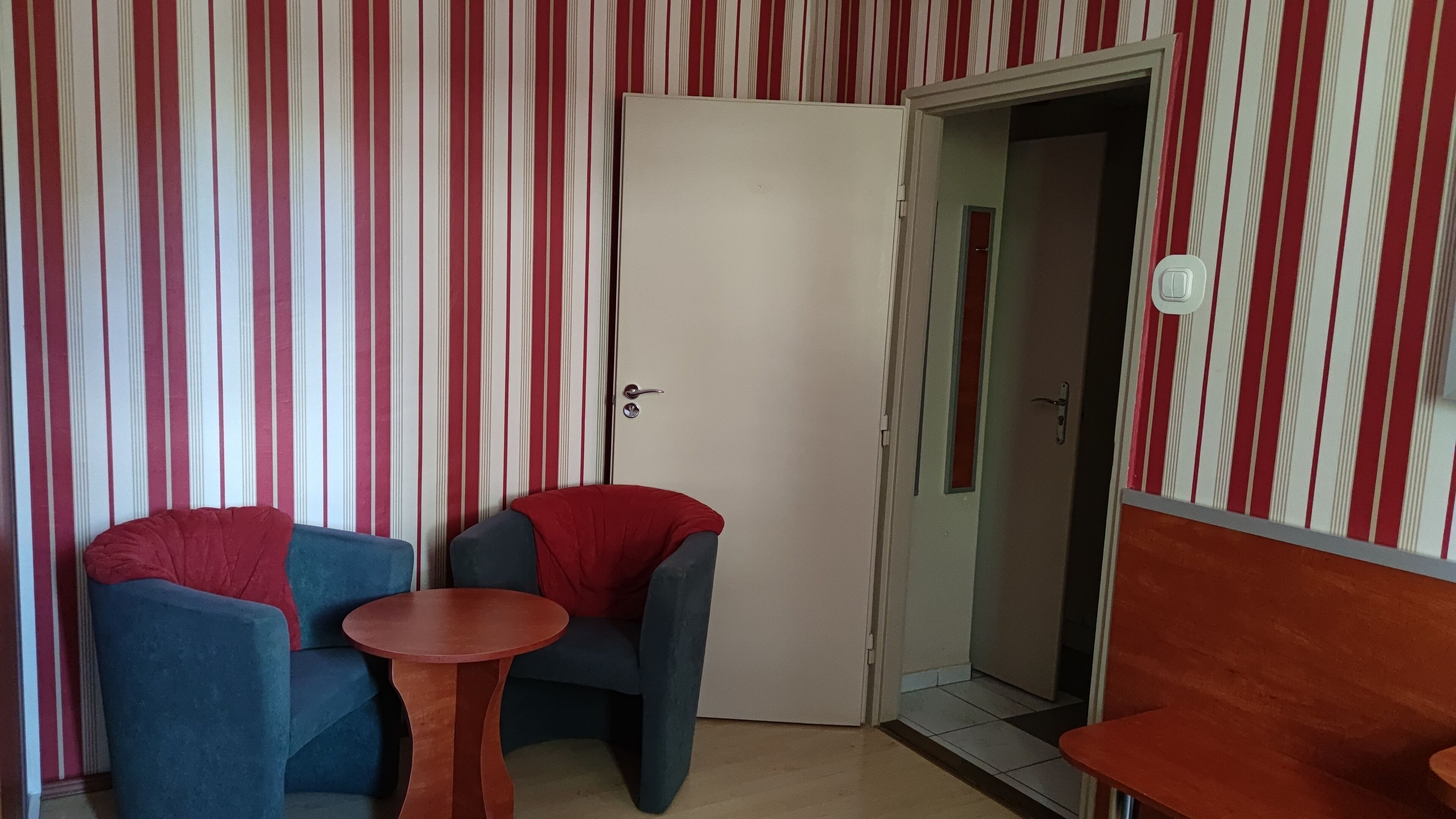 Una habitación con papel tapiz a rayas, una puerta blanca y dos sillones azules con cojines rojos.