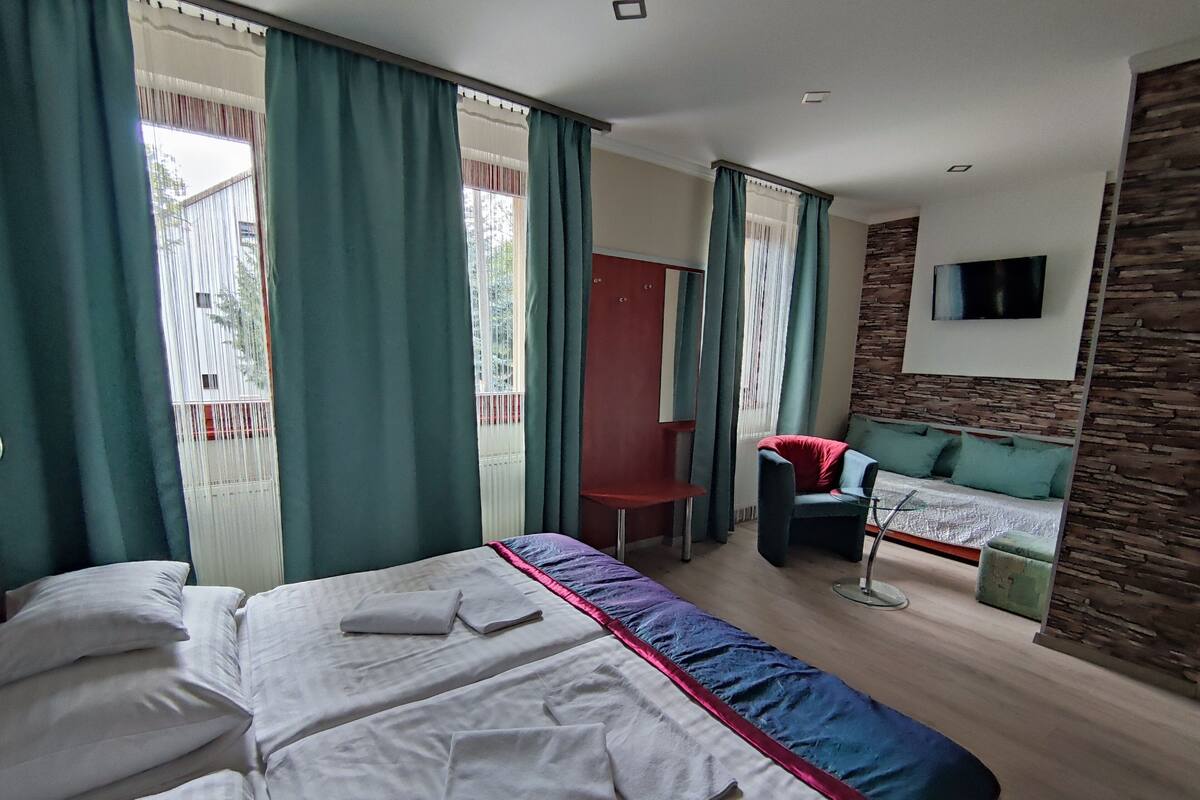 Habitación de hotel con dos camas, una silla roja, una mesita y un televisor montado en una pared de piedra.