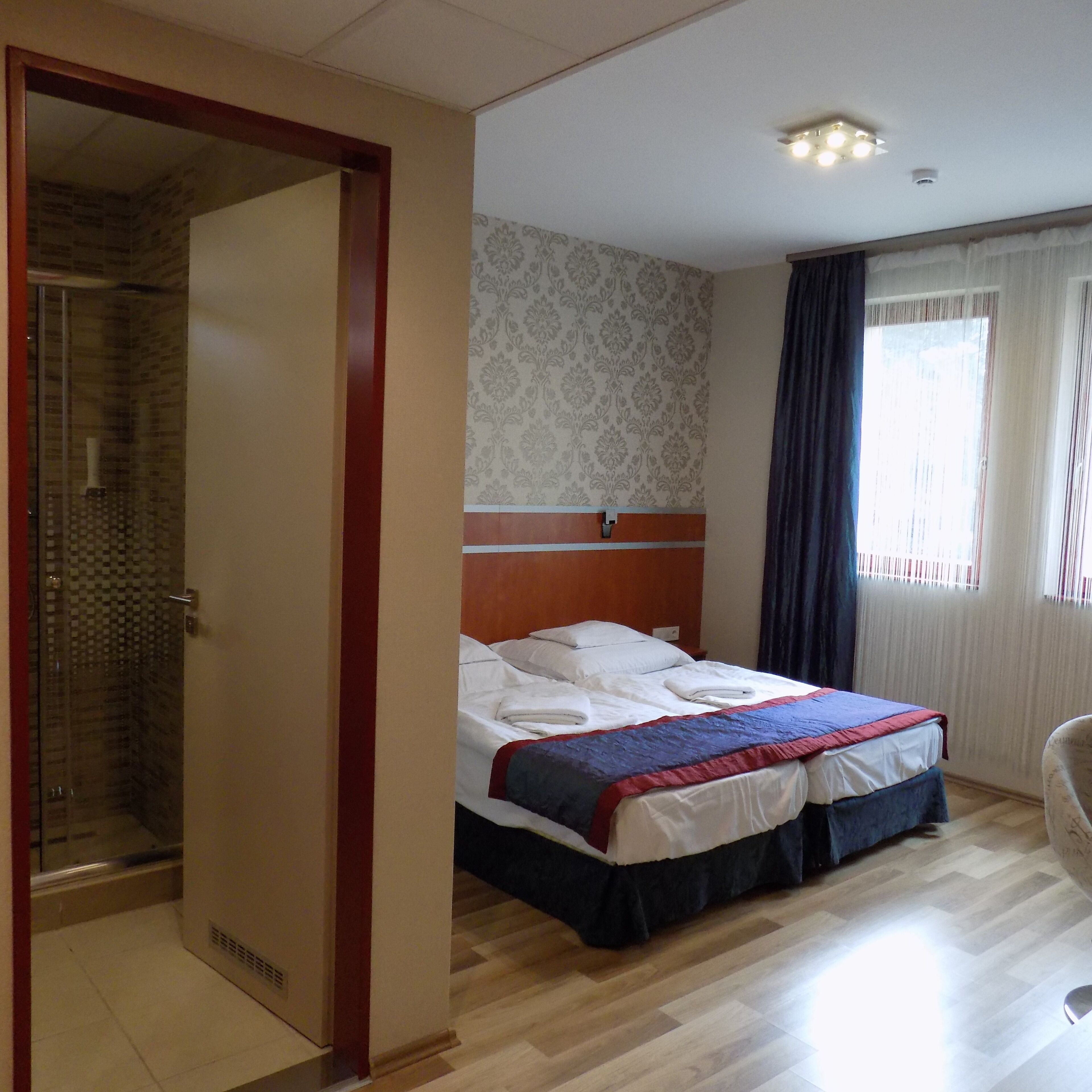 A hotel room with a bed, a shower, and a window with curtains.