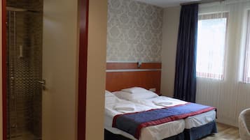 A hotel room with a bed, a shower, and a window with curtains.