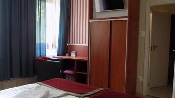 A hotel room with a bed, a desk, a television, and a door.