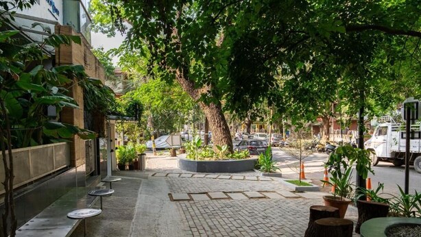 An outdoor seating area with tables and chairs, surrounded by potted plants and trees. - Stopover Backpackers Stay (Bengaluru)