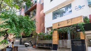 A courtyard with a restaurant named 'reachevents' and a 'Stop & Over' sign on a building. - Stopover Backpackers Stay (Bengaluru)