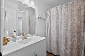 Un baño con tocador blanco, espejo, lavamanos y cortina de ducha con estampado de paisley.