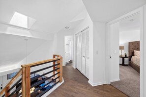 Een ruime hal met een houten trap, een slaapkamer met een bed en nachtkastje, en een kast met witte luiken.