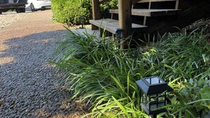 Una terrassa de fusta amb una escala que condueix a una zona coberta, envoltada de grava i vegetació.