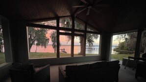 Un espacio de estar al aire libre cubierto con mobiliario de mimbre y ventanas amplias con vistas a una masa de agua.