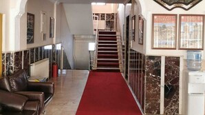 A hotel lobby with a red carpet, marble walls, a staircase, and a water dispenser.