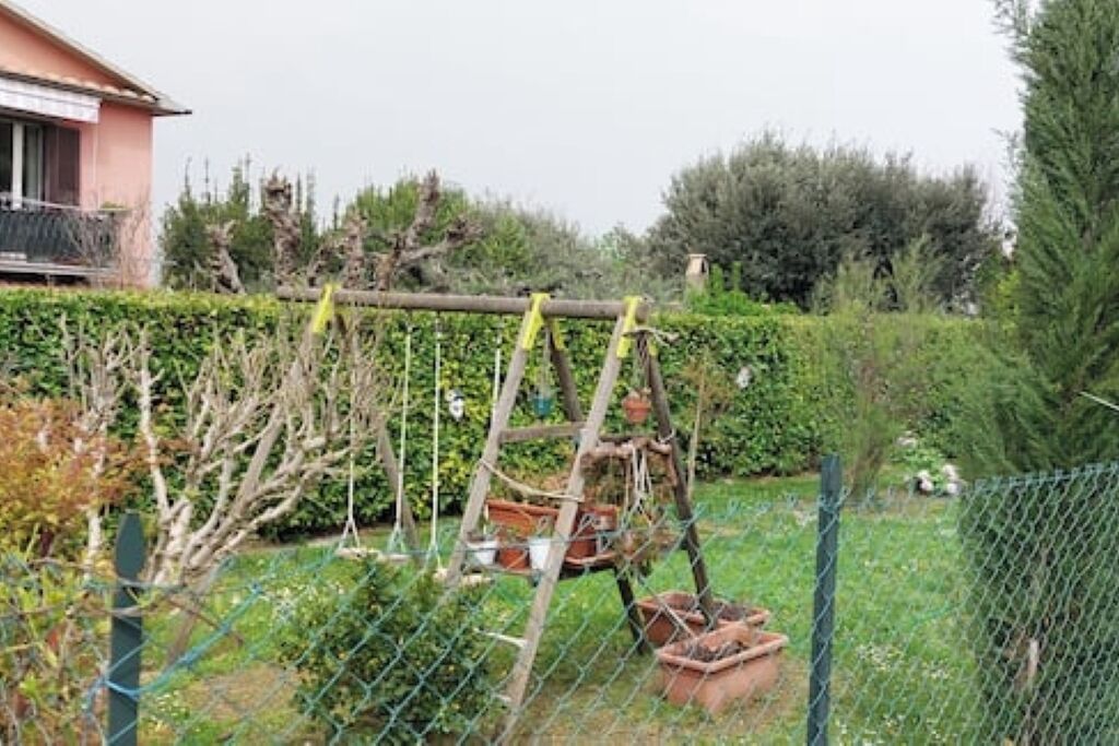 Un'area giardino recintata con una struttura in legno, probabilmente per piante rampicanti, e una casa sullo sfondo.