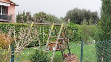 Un'area giardino recintata con una struttura in legno, probabilmente per piante rampicanti, e una casa sullo sfondo.