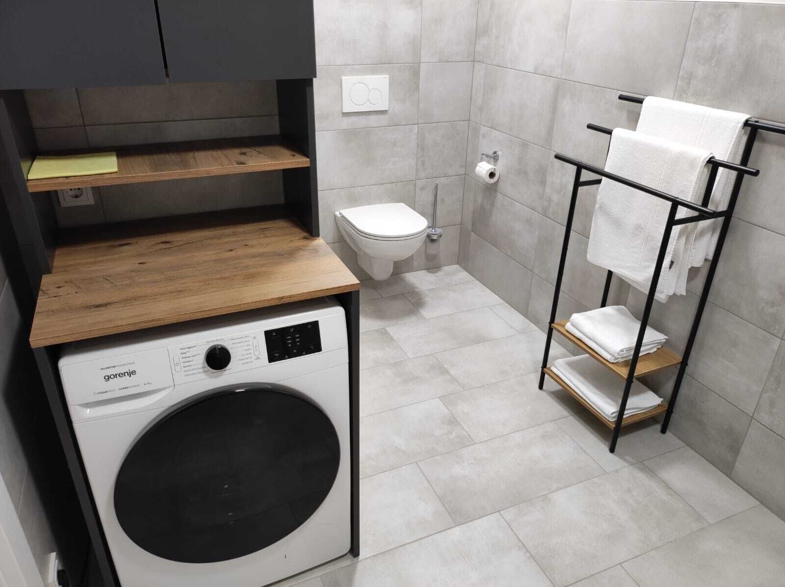 A compact bathroom with a washing machine, toilet, and towel rack.