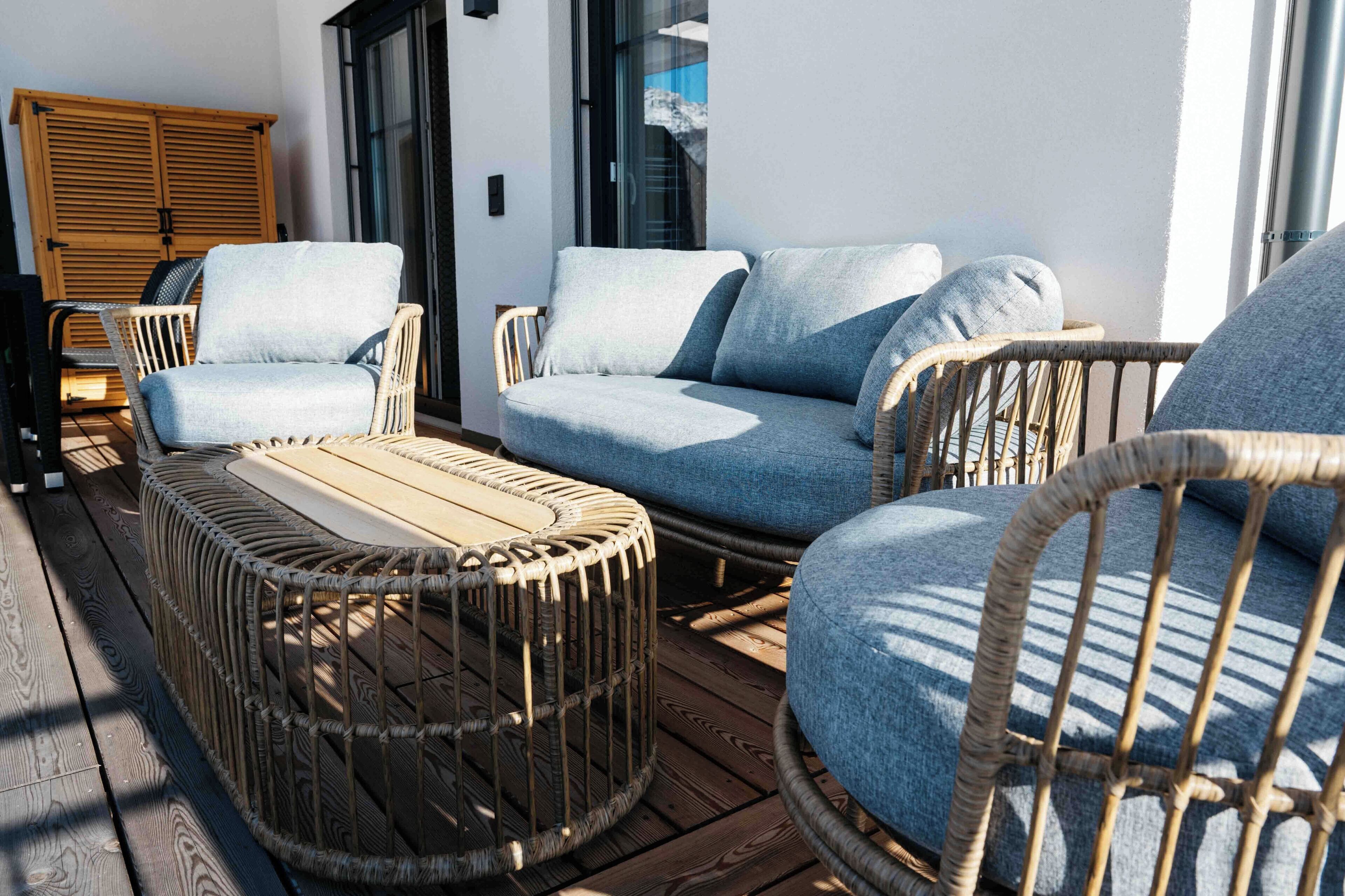 A wooden deck with wicker furniture, including a sofa and chairs, and a round table.