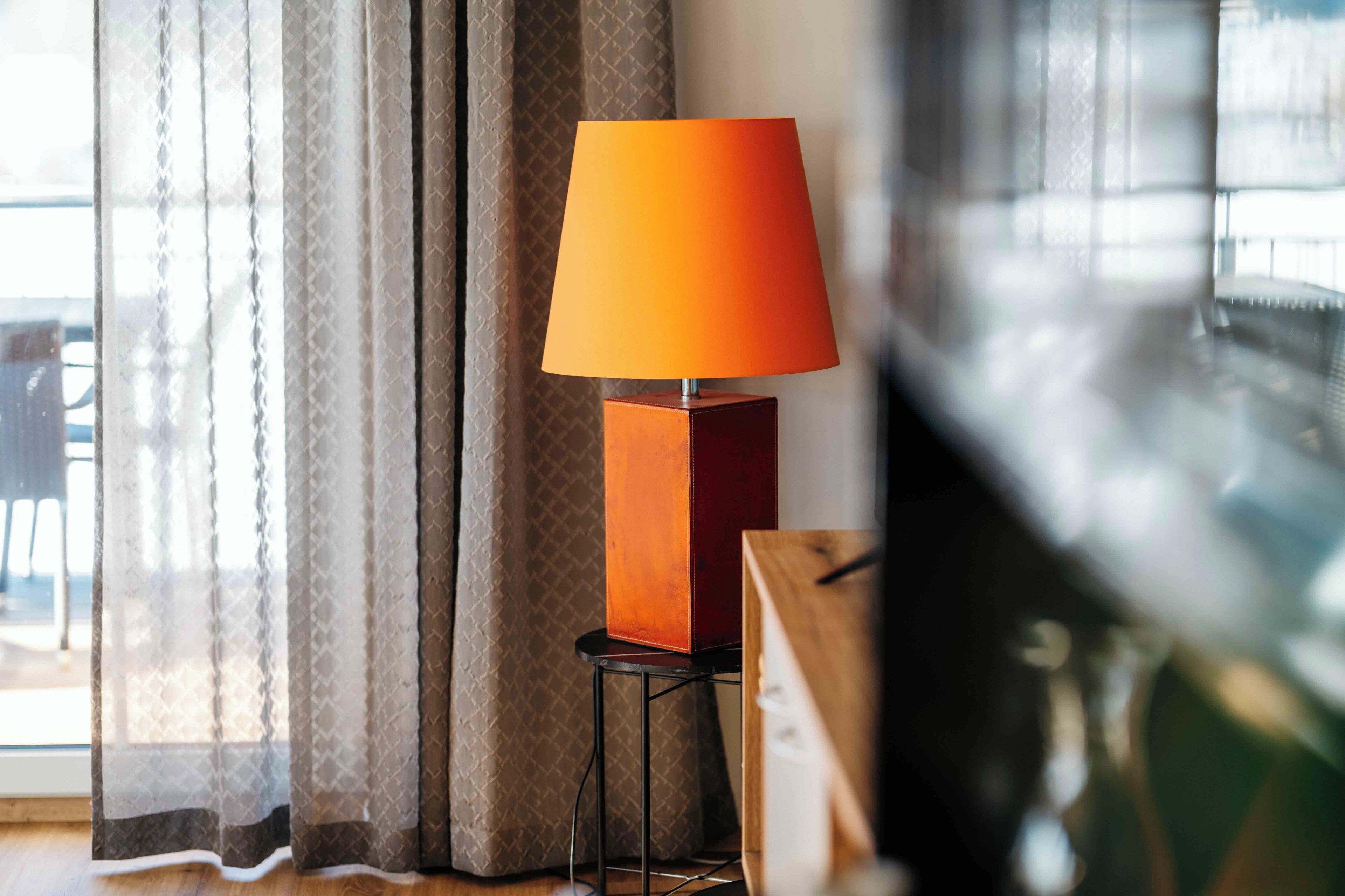 Une pièce avec un lampadaire, une table d’appoint en bois et une vue à travers des rideaux transparents.
