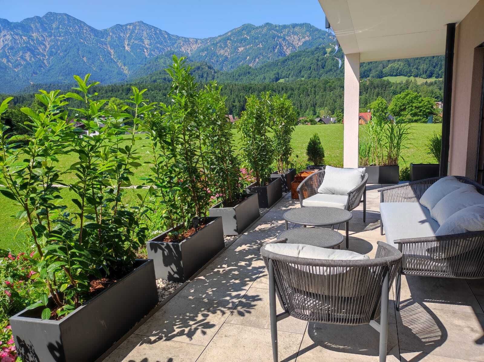 Een terras met tuinmeubilair, potplanten en uitzicht op bergen.