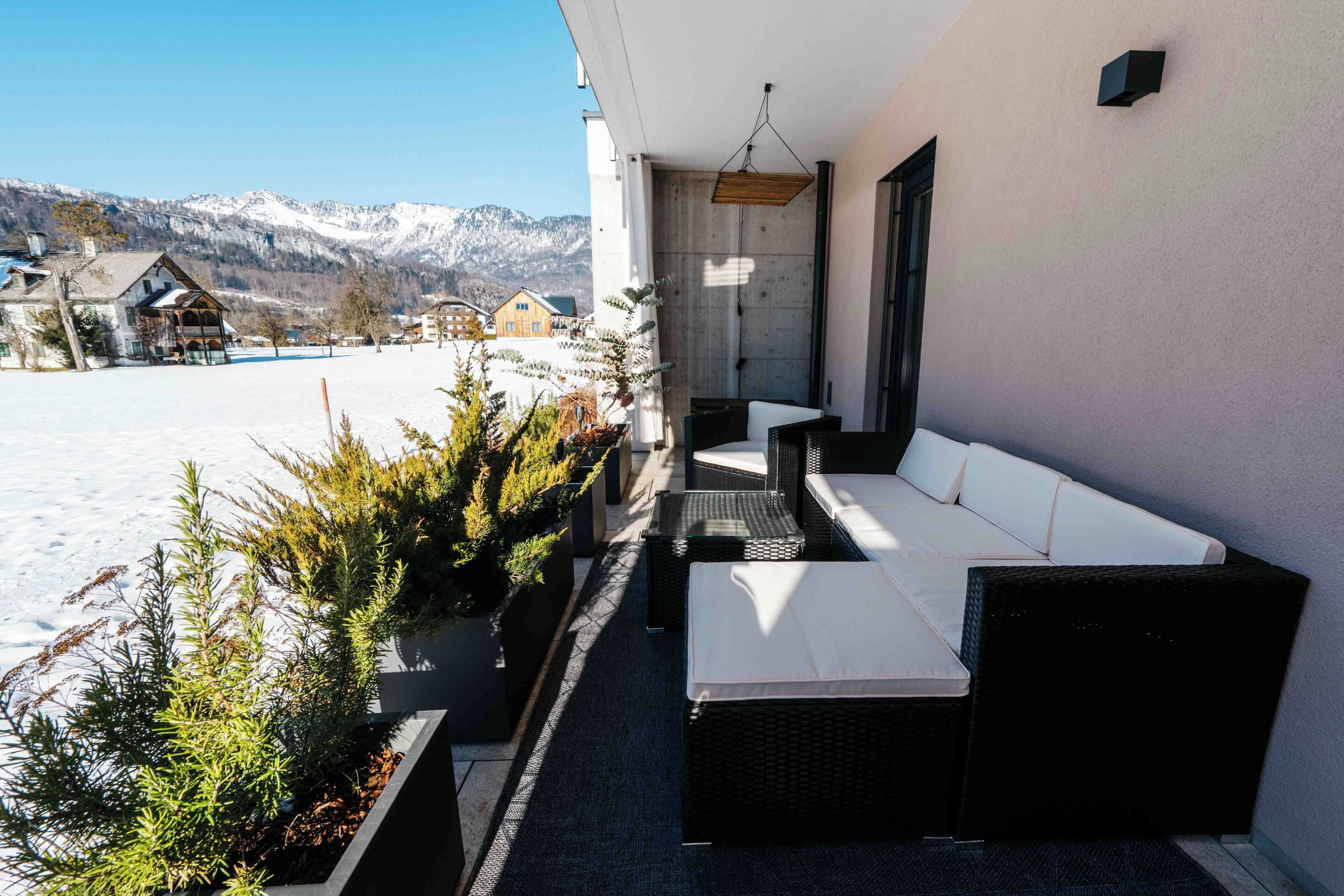 Ein Balkon mit einer Couch und einem Esstisch, mit Blick auf eine verschneite Landschaft mit Häusern und Bergen.