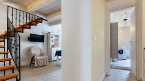 Una escalera con escalones de madera y barandillas negras, una pared blanca con un televisor montado, una silla con funda a rayas y un área de lavandería con lavadora.