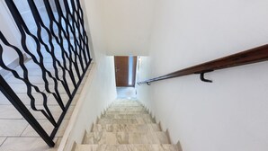 Una escalera con barandilla de metal negro, peldaños de mármol y pasamanos de madera.