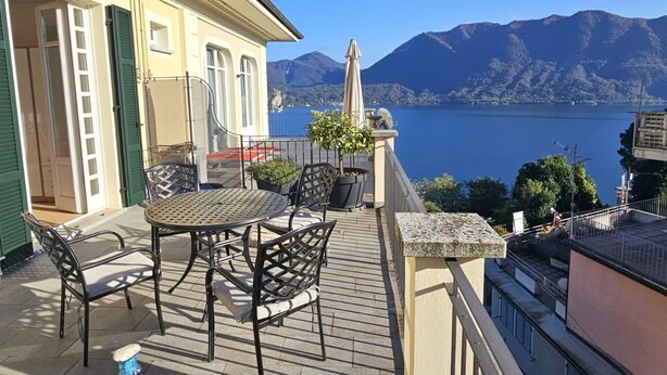 Een terras met een tafel en stoelen, met uitzicht op een meer en bergen.