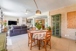 A dining area with a table set for four, a sofa, a television, and a cabinet with glassware.