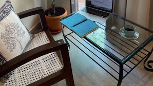 Een balkon met een laptop, een bloempot, een stoel en een glazen tafel met een beker.