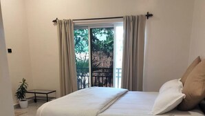 Een slaapkamer met een bed, gordijnen, een kamerplant en uitzicht op groen buiten.