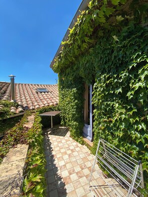 A courtyard with a tiled floor, a metal rack, and a building covered in ivy. - Lo Cantou" vacation home (Camplong-d'Aude)