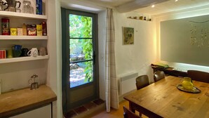 A cozy dining area with a wooden table and chairs, a window with curtains, and shelves with kitchen items.