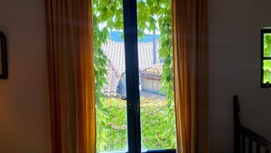 A room with a wooden door, curtains, a bed, and a potted plant.