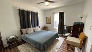 Ein Schlafzimmer mit einem Bett, einem Sessel, einem kleinen Tisch, einer Stehlampe und einem Deckenventilator.