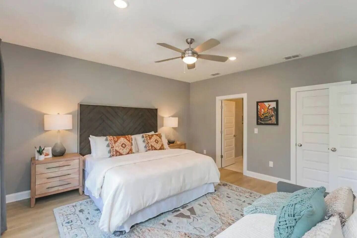 A bedroom with a bed, nightstands, a ceiling fan, and a door.