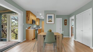 A modern kitchen with wooden cabinets, a dining table with chairs, and a view of the outdoors through a glass door. - Hot Tub, EV Charger, Plus Stunning Hill Country Stargazing & Wildlife (Spring Branch)